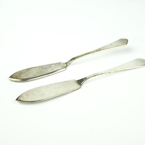May include: Two silver butter knives with rounded handles and pointed blades.