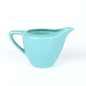 May include: A light blue ceramic creamer with a rounded handle.