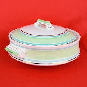 May include: A ceramic serving dish with a lid. The dish has pastel green, pink, and blue stripes, with gold trim. The handles and lid handle are white with green accents. A decorative piece for serving food, ideal for a dinner party.