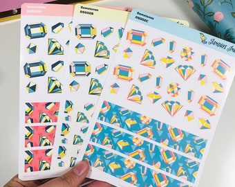 Op de afbeelding: Drie vellen met kleurrijke geometrische edelsteenstickers. De stickers tonen een verscheidenheid aan vormen en maten van edelstenen in roze, geel en blauw. De stickers zijn in rijen op de vellen gerangschikt. De vellen zijn gelabeld met "Gemstones" en hebben een productcode.