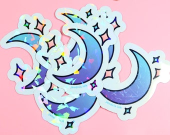 Op de afbeelding: Een set van vier iriserende holografische stickers met halve manen en sterren. De stickers zijn op een roze achtergrond.