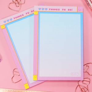 May include: Two pink and blue gridded notepad sets with the text "THINGS TO DO:" in a pixelated font. The notepads have a pink and blue gradient border with hearts and arrows.