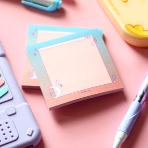 May include: Two pastel blue and pink sticky note pads with a moon and stars design. The top of the note pad has a browser window design. The note pad is labelled "Jandrich Ink".