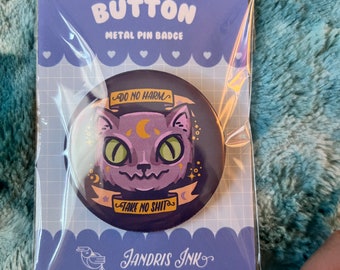 Op de afbeelding: Een ronde, zwarte knop met een afbeelding van een paarse kat met groene ogen en een halve maan op zijn kop. De knop heeft de tekst "Do No Harm" en "Take No Shit" in een wit, cursief schrift. De knop is verpakt in een doorzichtige plastic zak met een paarse en witte achtergrond waarop "Button Metal Pin Badge" en "Jandris Ink" staat.