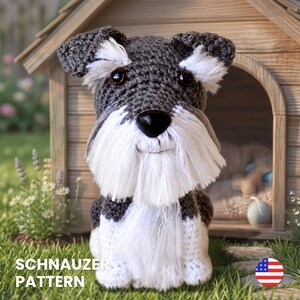 Pode incluir: Um brinquedo de cão Schnauzer feito em crochê com pelo cinza escuro na cabeça e orelhas, com detalhes de pelo branco ao redor dos olhos, focinho e peito. O brinquedo tem olhos castanhos escuros e nariz preto. Texto SCHNAUZER PATTERN visível.