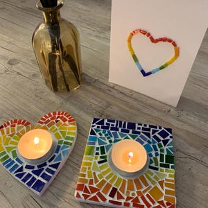 May include: Two rainbow mosaic heart-shaped candle holders with tealight candles. The candle holders are made of small pieces of glass in a rainbow pattern.