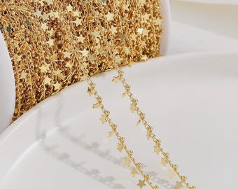 Op de afbeelding: Goudkleurige ketting met ster-vormige bedels. De ketting is opgerold, met twee strengen die naar beneden lopen. De sterren zijn gelijkmatig verdeeld, waardoor een delicaat ontwerp ontstaat. De ketting wordt waarschijnlijk gebruikt voor het maken van sieraden.