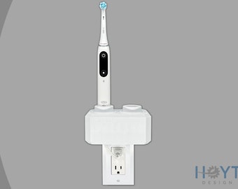 Puede incluir: Cepillo de dientes eléctrico blanco con un cabezal de cepillo azul, montado en una estación de carga blanca que se conecta a una toma de corriente estándar. La estación de carga tiene una segunda ranura para un segundo cepillo de dientes.