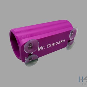 May include: A magenta-colored cylindrical object with four suction cups attached. The text "Mr. Cupcake" is printed on the side. The object appears to be a holder or container.