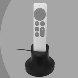 Puede incluir: Un mando a distancia blanco con botones grises y un panel de control circular se coloca en un soporte negro. El mando a distancia tiene un botón de encendido y otros botones de función. El soporte tiene un diseño redondeado en forma de cono.