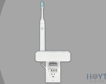 Puede incluir: Cepillo de dientes eléctrico blanco cargando en un tomacorriente de pared blanco con un estante blanco. El estante tiene un tomacorriente integrado con tres puertos USB.