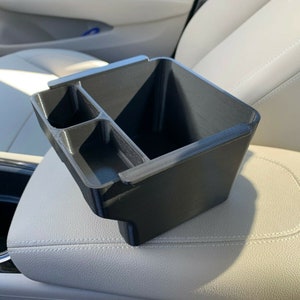 May include: Black plastic car organizer with three compartments. The organizer is designed to fit in the center console of a car.