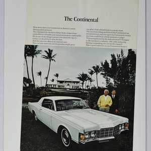 May include: A white 1969 Lincoln Continental saloon parked on a grassy driveway in front of a white house with palm trees. The car has a black interior and a chrome bumper. The text "The Continental" is at the top of the image. The text "LINCOLN-MERCURY Ford" is at the bottom of the image.
