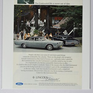 May include: A vintage advertisement for the Lincoln Continental car. The ad features a black and white photo of a 1965 Lincoln Continental sedan driving down a street lined with trees. The text reads "The Continental life is never out of date." and "Come live the Continental life."