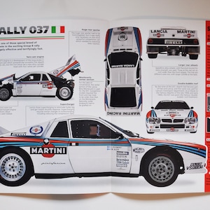 May include: A white and blue Lancia Rally 037 Evo 2 race car with Martini Racing sponsorship. The car has a large rear wing and a double bubble roof. The car is on a white background with text about the car's specifications.