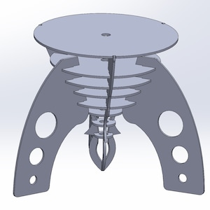 Op de afbeelding: Een grijze, lasergesneden houten tafel met een rond blad en drie poten. De poten zijn ontworpen met een reeks overlappende cirkels en een puntige onderkant.