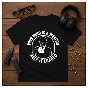 May include: Black t-shirt with a white graphic of a person aiming a gun, encircled by the text "YOUR MIND IS A WEAPON KEEP IT LOADED." Accessories include black headphones, yellow-tinted sunglasses, and two black magazines.