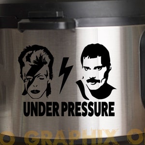 以下が含まれることがあります： 黒いアクセントが付いたステンレス鋼の電気圧力鍋。デヴィッド・ボウイとフレディ・マーキュリーの黒いシルエットグラフィック、稲妻、そして「UNDER PRESSURE」の文字が特徴です。楽しいキッチン家電です。