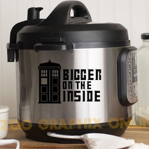 Può includere: Una pentola a pressione elettrica in acciaio inossidabile con coperchio e manico neri. Un adesivo bianco e nero sul lato della pentola a pressione presenta una silhouette del TARDIS di Doctor Who e il testo "BIGGER ON THE INSIDE".