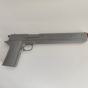 Può includere: Una replica di pistola stampata in 3D di colore grigio con una canna lunga e una punta arancione. Sul lato della canna è inciso il testo Hellsing Arms Weapon, Casull 454 e Industrial Ltd. L'arma presenta un'impugnatura testurizzata e finitura metallica.