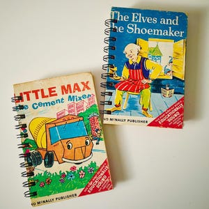 May include: Two spiral-bound books with illustrated covers. One features a yellow cement mixer truck titled Little Max the Cement Mixer. The other shows a shoemaker at a workbench titled The Elves and the Shoemaker. Both include Rand McNally Publisher text.