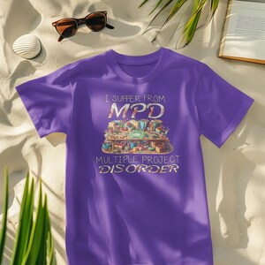 Może przedstawiać: Fioletowy T-shirt z grafiką stołu z różnymi materiałami do rękodzieła i tekstem "I suffer from MPD Multiple Project Disorder".