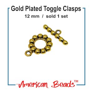 May include: Gold-plated toggle clasps, 12 mm in size, are displayed against a white background. The clasps are a warm gold color and consist of a circular piece with a series of small, round beads and a bar with a loop. The text "Gold Plated Toggle Clasps" is at the top.