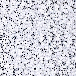 May include: Close-up of a pile of small, translucent white seed beads. The beads are round with a hole through the center, and they are scattered across the frame. The beads are used for jewelry making and crafts.