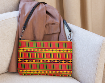 Puede incluir: Un bolso bandolera con estampado geométrico rojo, amarillo, verde y negro con una correa negra.