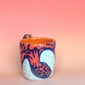 on white speckle clay, I have carved an image of a two headed snake design of mine- the inside color is bright orange, just like the eyes of the snakes, and the snakes are dark blue. they're scales/flame markings are colored with a mixture of different oranges