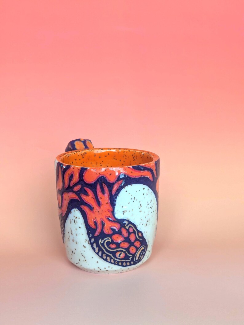 on white speckle clay, I have carved an image of a two headed snake design of mine- the inside color is bright orange, just like the eyes of the snakes, and the snakes are dark blue. they're scales/flame markings are colored with a mixture of different oranges