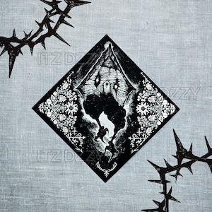 May include: Black and white illustration of a haunted house within a diamond shape, surrounded by floral patterns and a thorny crown design. The artwork is set against a gray linen background, creating a gothic or dark aesthetic.