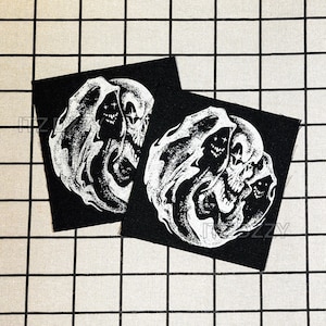May include: Two black square patches with a white illustration of a skull with a flowing, ghostly design. The skull has visible teeth and eye sockets. The patches are placed on a checkered, off-white background.