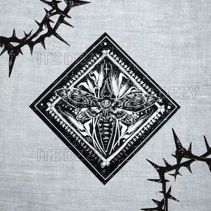 May include: Black and white diamond-shaped graphic featuring a moth with a skull-like design, surrounded by floral elements and a cross. The image is set against a gray, textured background, with thorny branches in the corners.
