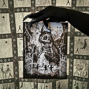 May include: A black and white print featuring a skeletal figure with a horned head, set against a backdrop of a full moon and bare trees. The print includes a gate and dancing figures, creating a gothic theme.