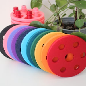 May include: A set of colourful round foam pieces with holes in the centre. The pieces are stacked in a rainbow order, starting with black and ending with red.