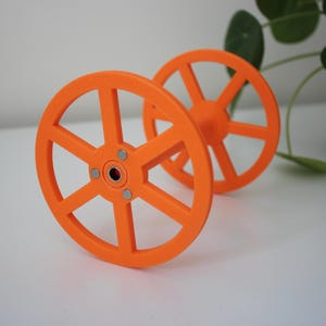 May include: Two bright orange plastic spools with a centre hole and six spokes on each spool.
