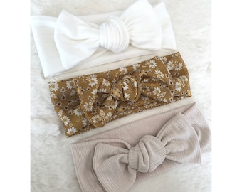 May include: Three fabric headbands with different patterns. The top headband is white, the middle headband has a floral pattern in shades of yellow and brown, and the bottom headband is a light beige.