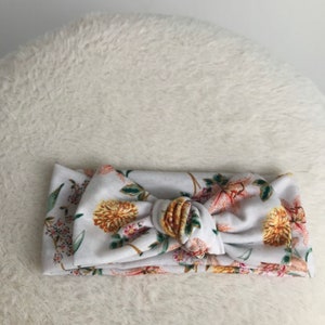 Pode incluir: Uma faixa de cabe&ccedil;a branca com estampa floral em tons de rosa, amarelo e verde. A faixa de cabe&ccedil;a &eacute; amarrada em um n&oacute; na parte superior.