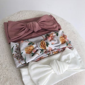 Pode incluir: Tr&ecirc;s faixas de cabelo de tecido com la&ccedil;os atados. Uma faixa &eacute; de cor rosa p&oacute; s&oacute;lida, outra &eacute; branca com estampa floral e a &uacute;ltima &eacute; branca s&oacute;lida.