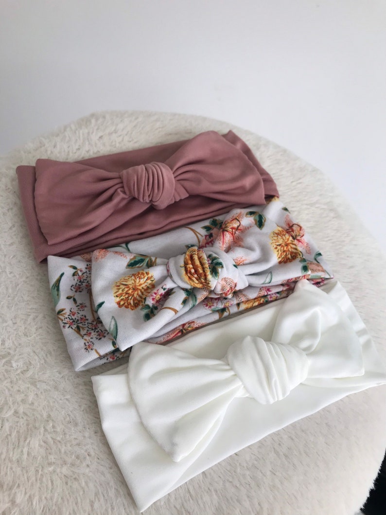Pode incluir: Tr&ecirc;s faixas de cabelo de tecido com la&ccedil;os atados. Uma faixa &eacute; de cor rosa p&oacute; s&oacute;lida, outra &eacute; branca com estampa floral e a &uacute;ltima &eacute; branca s&oacute;lida.