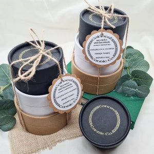 May include: A set of three black and brown round candle containers with gold labels. The labels have the text "Coinneal Candle Co." and list the scents "Coal Grey Tea & Cucumber", "Midnight Berries", and "Star anise & Rose".