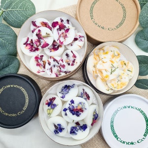 May include: Assortment of wax melts in round containers. The wax melts are white and contain dried flowers and herbs. The containers are labeled "Coinneal Candle Co."