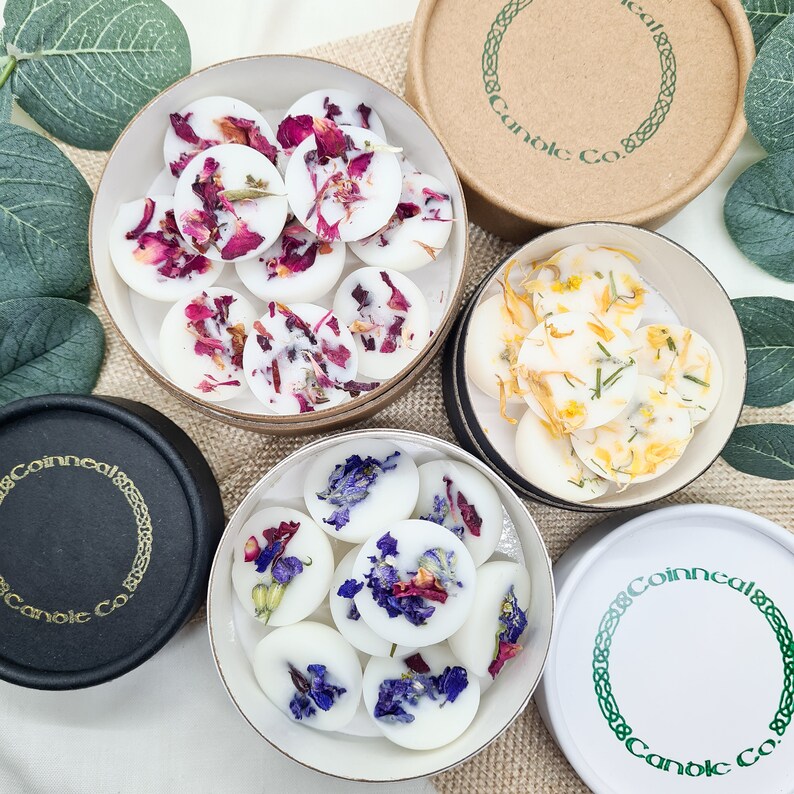 May include: Assortment of wax melts in round containers. The wax melts are white and contain dried flowers and herbs. The containers are labeled "Coinneal Candle Co."