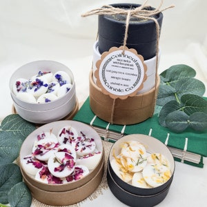 May include: Three round containers of wax melts with botanicals. The containers are stacked on top of each other. The top container is black, the middle container is white, and the bottom container is brown. The wax melts are in different colors and have different botanicals in them. The wax melts are labeled with the text "Coincal & Candle Co.", "wax melts with botanicals", "coconut & apricot wax", "cool grey tea & cucumber", "midnight berries", "rhubarb & anise".