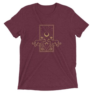 Może przedstawiać: Bordowy t-shirt z złotym wzorem graficznym przedstawiającym dwie pantery zwr&oacute;cone do siebie, nad kt&oacute;rymi znajduje się sierp księżyca i gwiazdy.