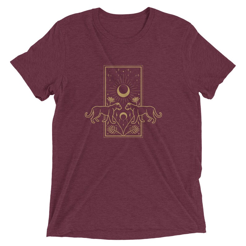 Może przedstawiać: Bordowy t-shirt z złotym wzorem graficznym przedstawiającym dwie pantery zwr&oacute;cone do siebie, nad kt&oacute;rymi znajduje się sierp księżyca i gwiazdy.