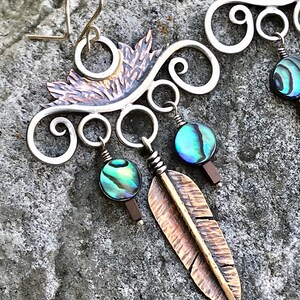 May include: Silver and copper earrings with a feather design and abalone shell accents. The earrings are handmade and feature a delicate, intricate design.