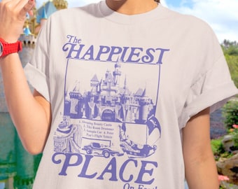May include: A white t-shirt with a purple graphic print of Sleeping Beauty Castle and the text "The Happiest Place on Earth".