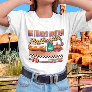 Op de afbeelding: Wit T-shirt met een kleurrijke afbeelding van een trein en de tekst "Big Thunder Mountain Railroad - 79 - Frontierland".
